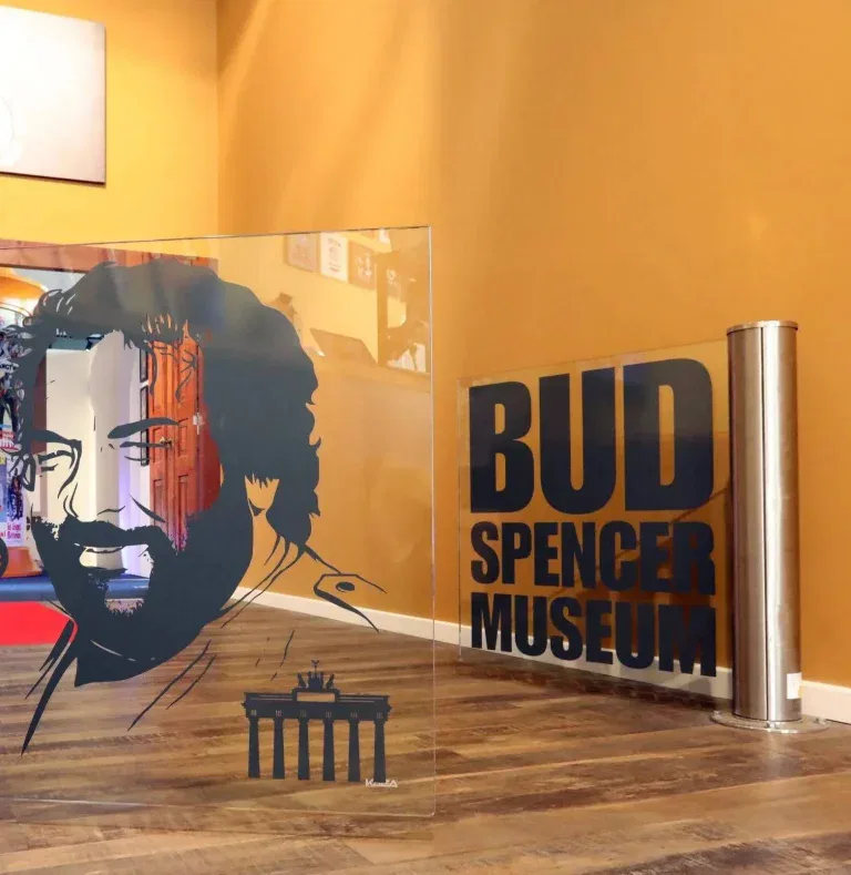 Ein Glasschild mit dem Porträt eines bärtigen Mannes und dem Brandenburger Tor steht neben einem Schild mit der Aufschrift 