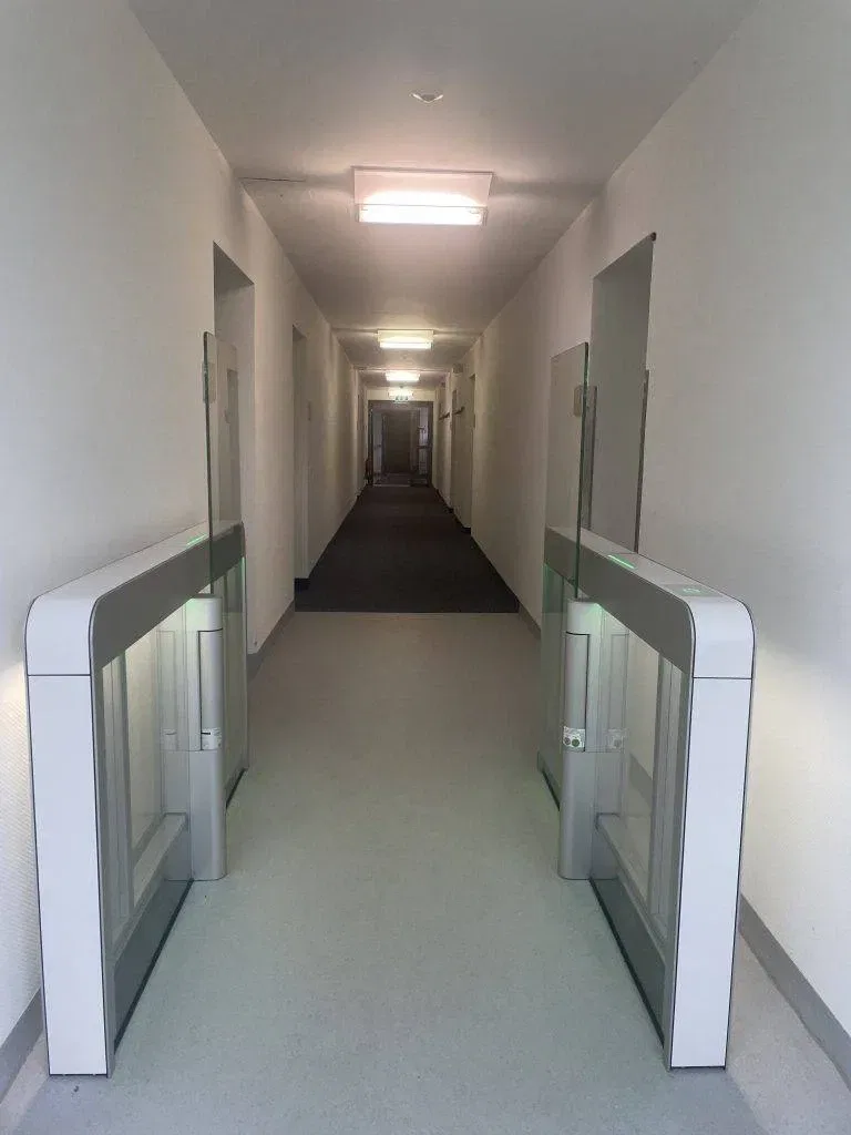 Ein langer, heller Flur mit weißen Wänden und Türen auf beiden Seiten, mit zwei modernen Sicherheitstoren in der Nähe des Eingangs.